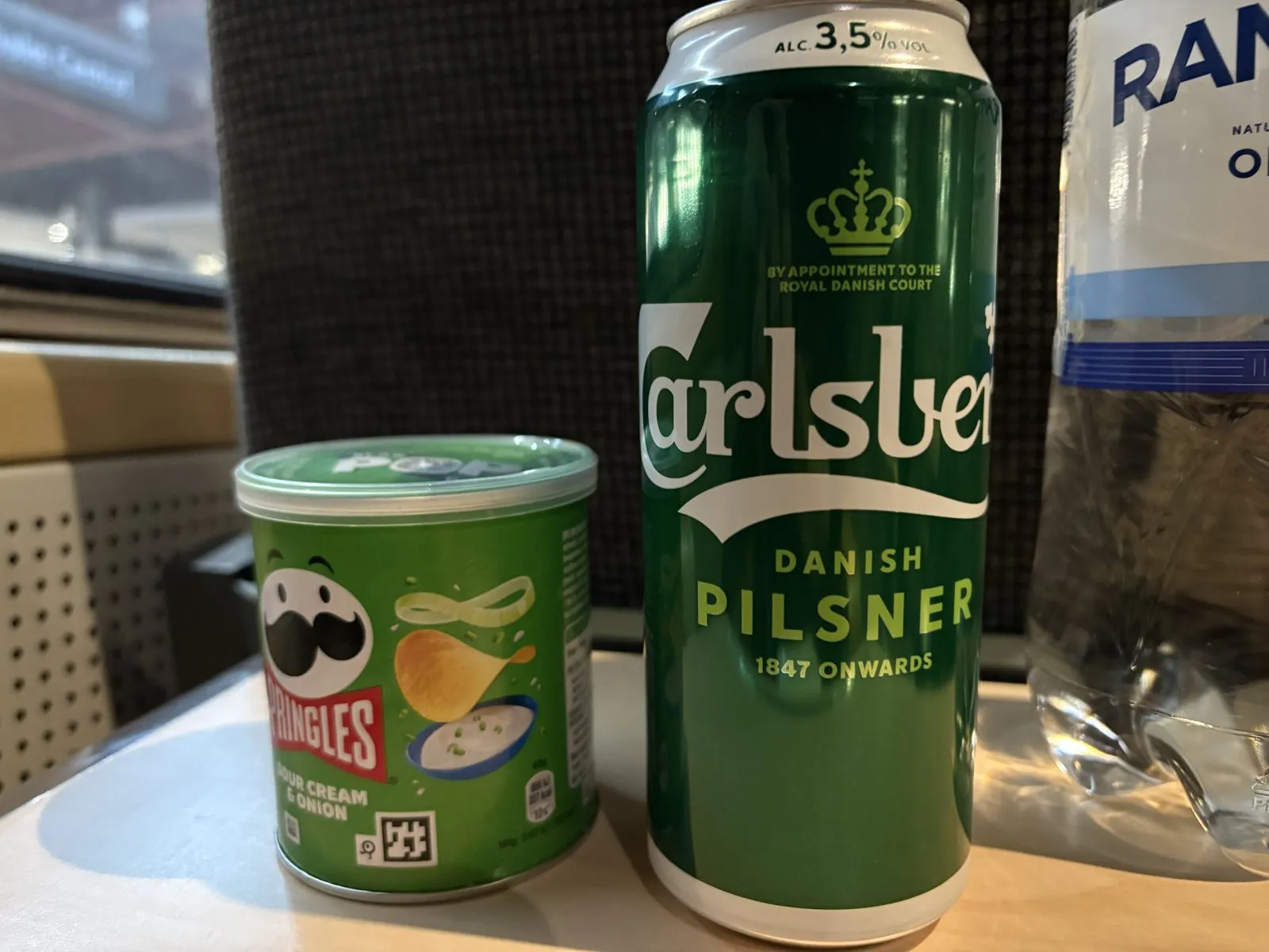 夜行列車の座席テーブルに置いた、プリングルスとカールスバーグの缶ビール