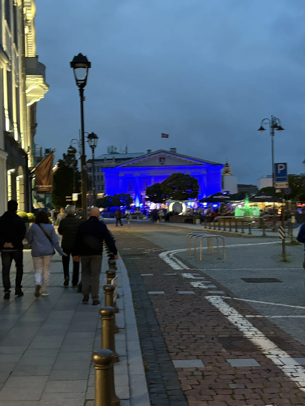 夜のヴィリニュスの通り。街灯が並び、奥の建物が青くライトアップされている